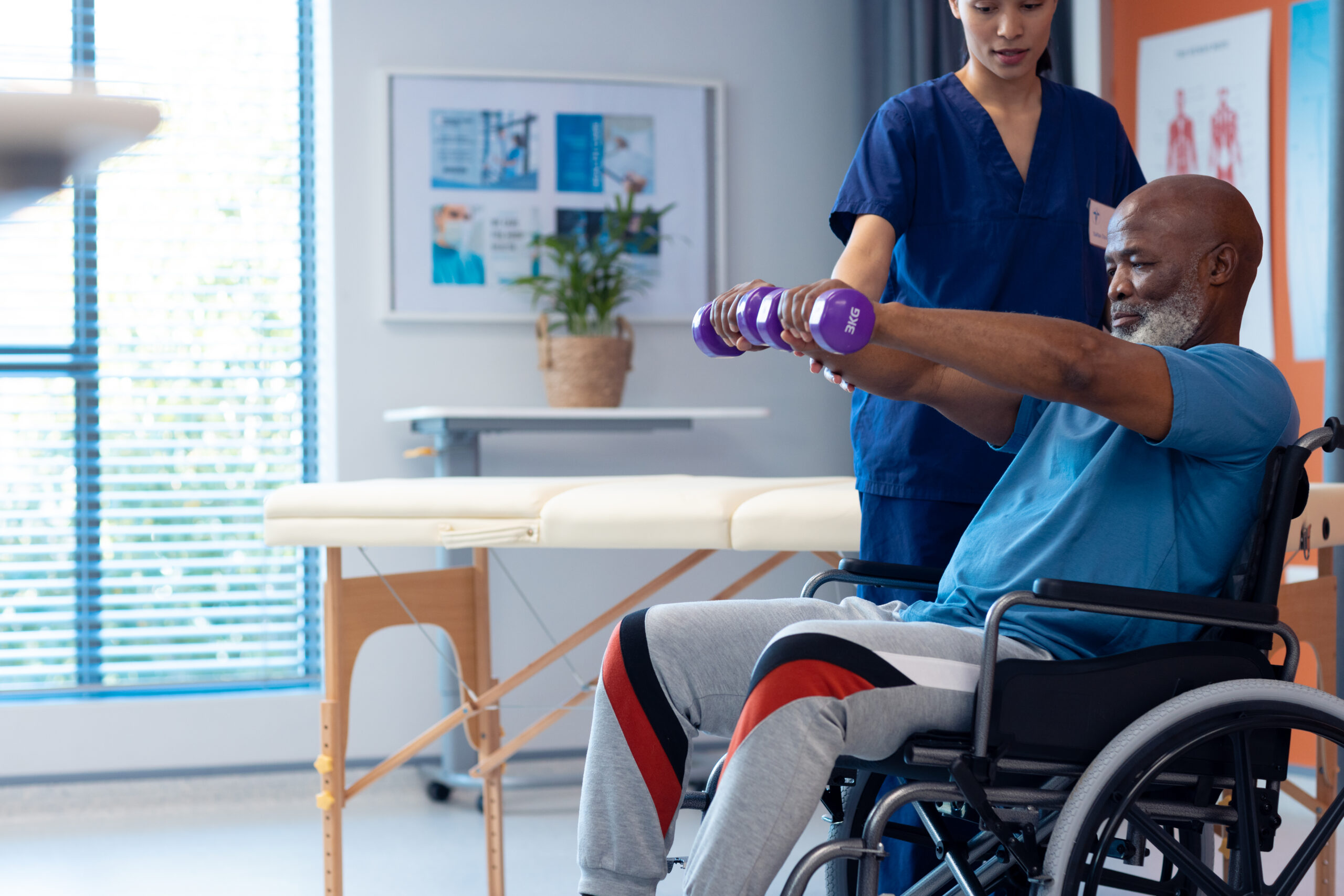 Diverse female physiotherapist helping senior male patient in wheelchair using dumbbells, copy space. Hospital, medical and healthcare services.