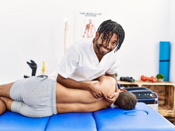 Two men physiptherapist and patient having rehab session massaging back at clinic